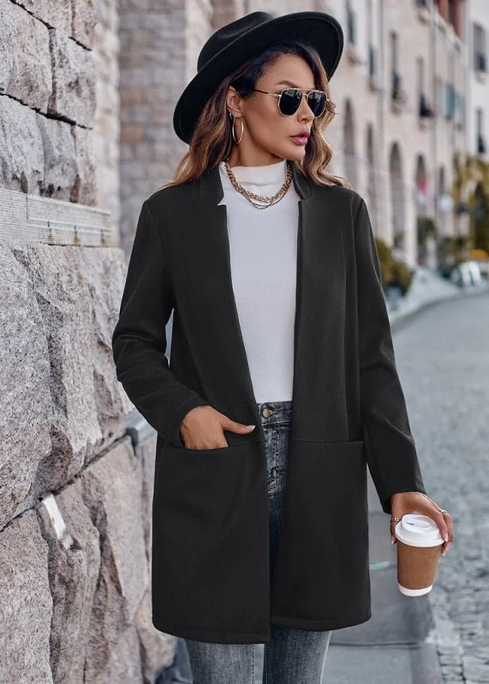 Black blazer with a relaxed fit, worn over a white turtleneck and jeans, holding a coffee cup.