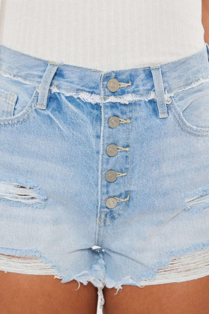 Close-up of light wash distressed denim shorts with a button fly and frayed hem.
