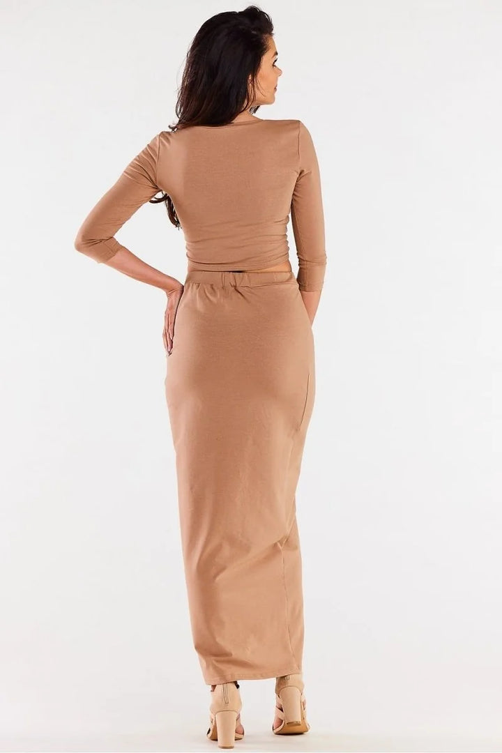 Back view of a woman wearing a beige long-sleeve crop top and a matching fitted maxi skirt.