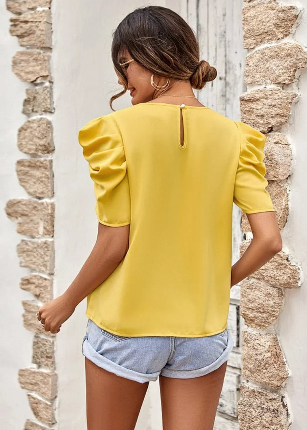 Back view of a bright yellow top with puffy short sleeves, paired with light wash denim shorts.