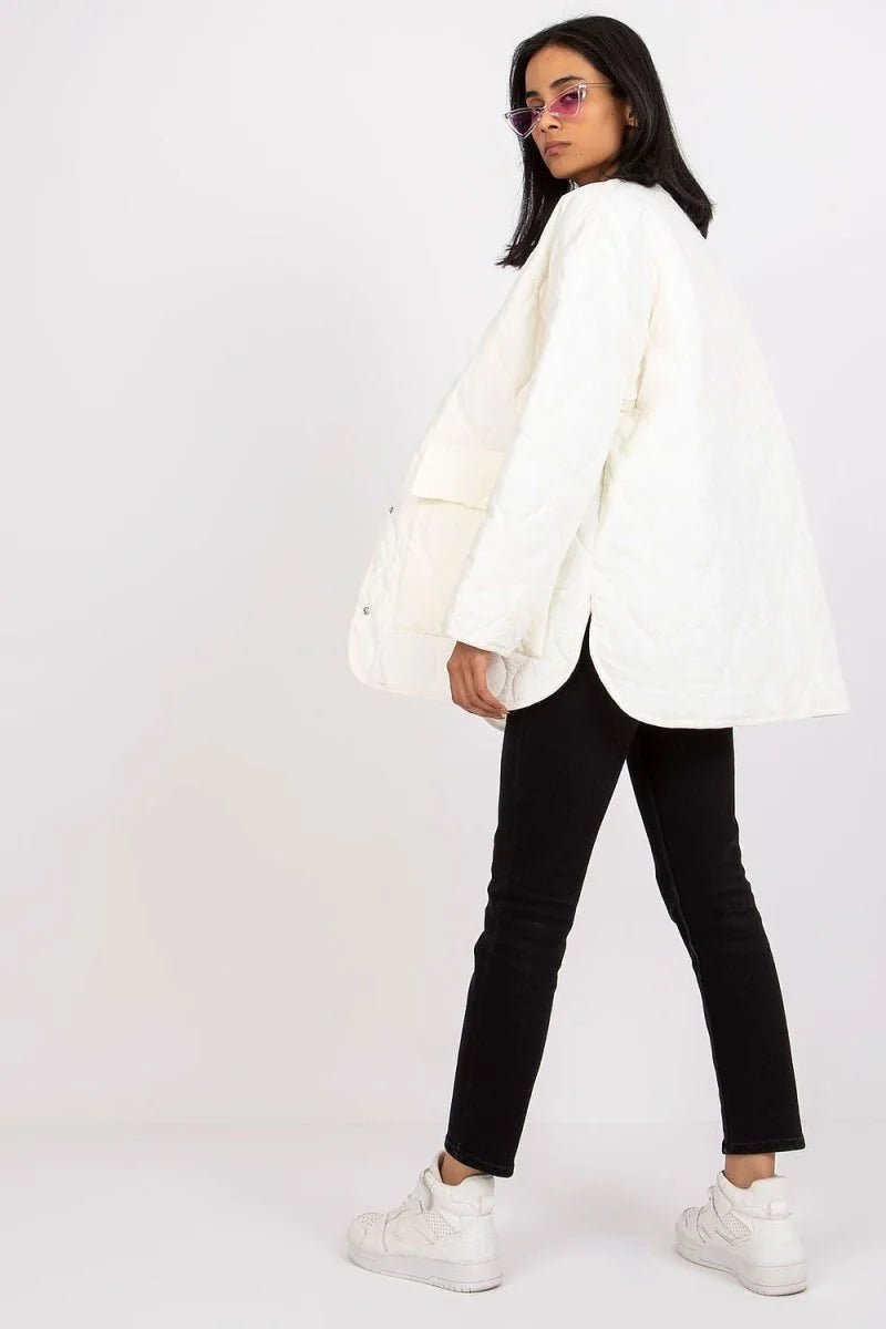 Cream quilted jacket with rounded hem and button closure, worn by a model with black jeans.