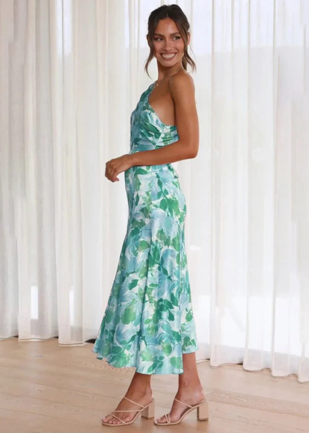 Full length view of a woman wearing a green and blue floral print, one-shoulder midi dress.