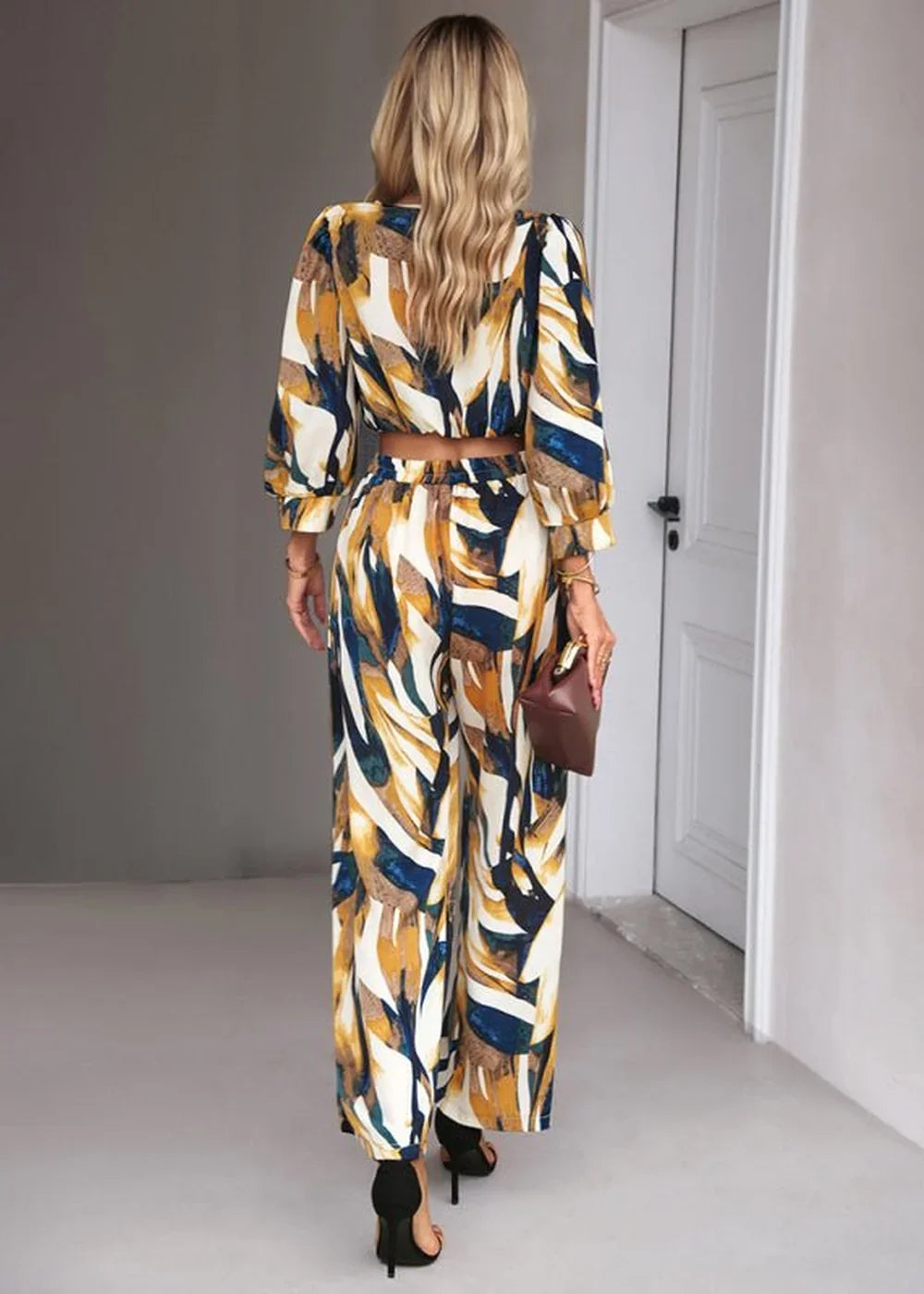 Woman in a colorful abstract print crop top and wide-leg pants, holding a brown clutch.